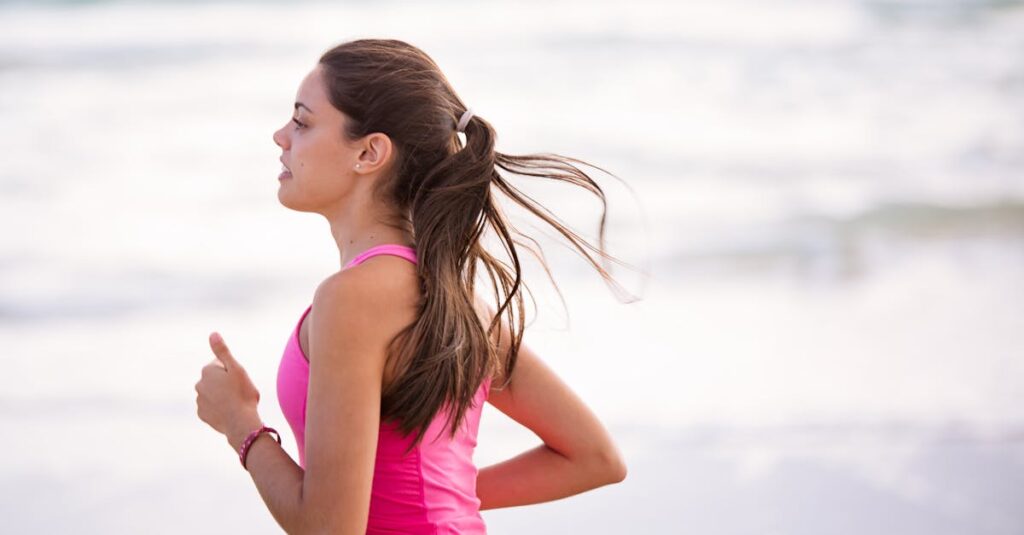 Side view of a young woman jogging on a beach wearing pink active wear.