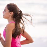 Side view of a young woman jogging on a beach wearing pink active wear.